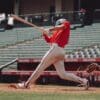 woman in red jersey shirt and white shorts holding baseball bat