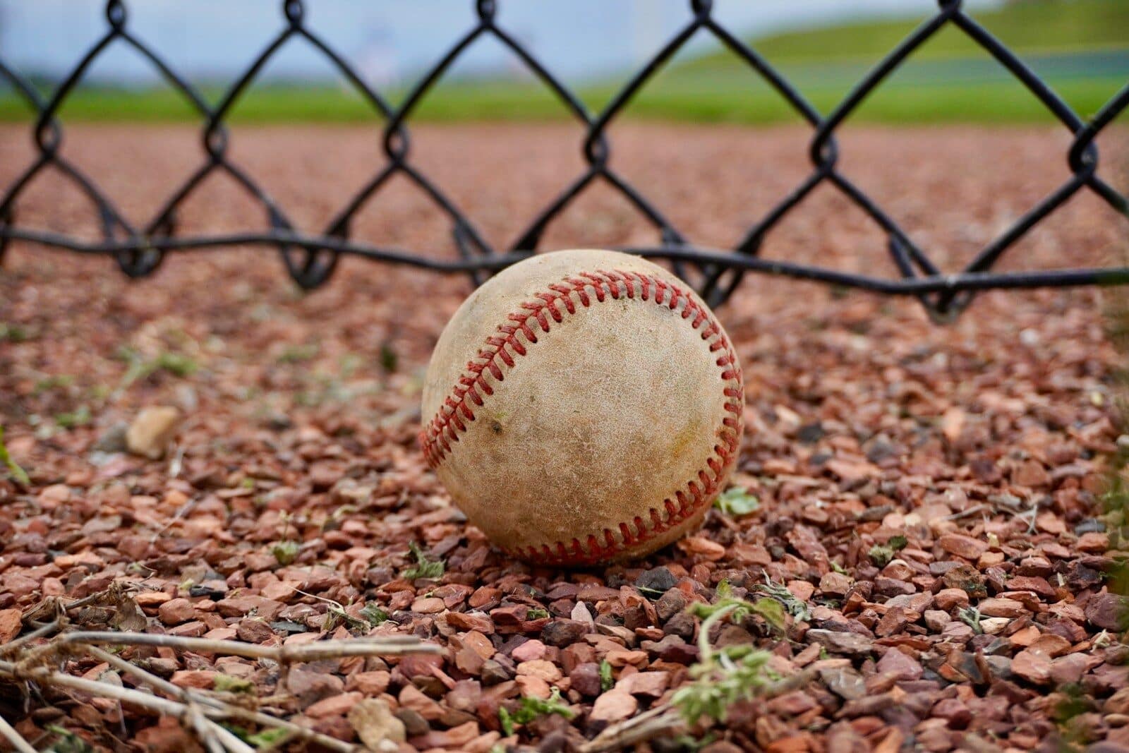 A baseball sits on the ground by a fence